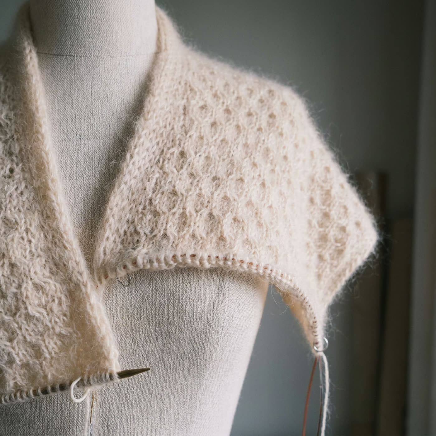 An unfinished knitted piece resting on a dress form, needles still attached
